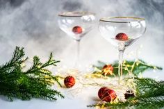 two wine glasses sitting on top of a table next to evergreen branches and red balls