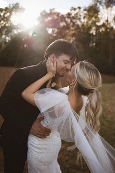 a bride and groom kissing in front of the sun with their veil blowing around them