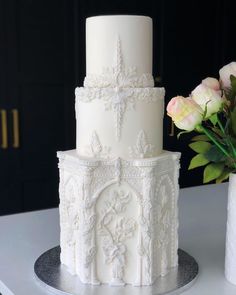 a three tiered white wedding cake sitting on top of a table next to two vases