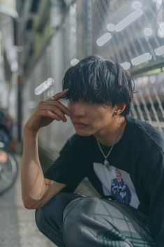 a young man sitting on the ground with his hand to his face and looking down