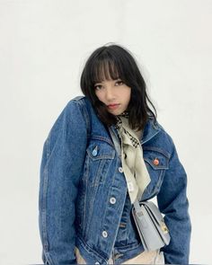 a young woman wearing a denim jacket and scarf standing in front of a white wall