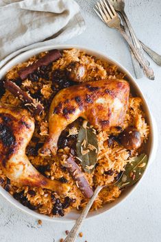 a white bowl filled with chicken and rice on top of a table next to silverware