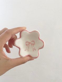 a hand holding a small white plate with a bow design on it's side