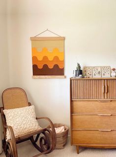 a wooden rocking chair next to a dresser with a painting on the wall above it