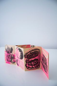 an open book with pink and black designs on the pages, sitting on a white surface