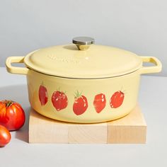 a yellow casserole dish with tomatoes on the side next to it and a wooden block