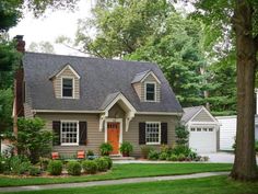 a gray house with white trim and brown shutters on the front door is surrounded by green grass