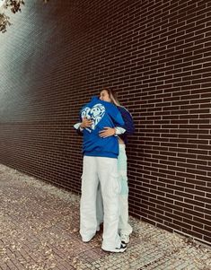 a person leaning against a brick wall with their arms around each other while wearing white pants and a blue hoodie