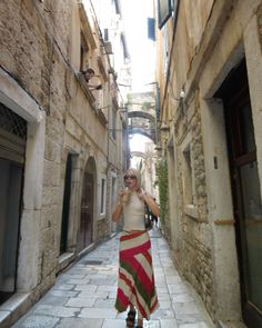 a woman is walking down an alleyway talking on her cell phone while wearing a striped skirt