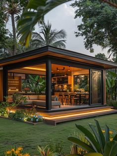 a small house is lit up at night in the yard with plants and flowers around it