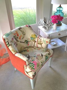 a colorful chair sitting in front of a window next to a table with flowers on it