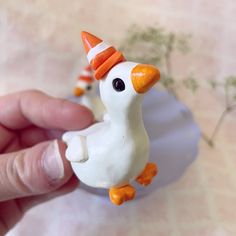 a hand holding a small toy duck with an orange hat