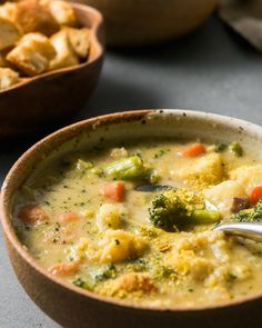 a bowl of soup with broccoli, carrots and potatoes in it next to a bowl of croutons