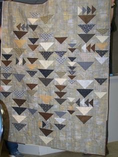 a person holding up a large quilt made with squares and triangles in grey, brown and white colors