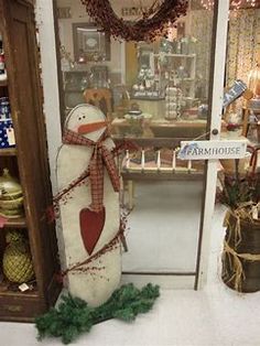 a snowman statue in front of a store window with christmas wreaths around it