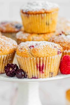 some blueberry muffins on a white plate with berries and powdered sugar