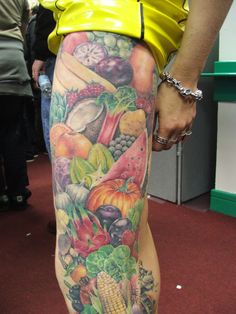 a person with tattoos on their legs is standing in front of a table full of fruit and vegetables