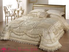 the bed is made up with white sheets and ruffled bedspread, along with gold trimmings