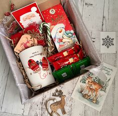 a christmas gift box filled with coffee mugs, cards and other holiday decorations on top of a wooden table