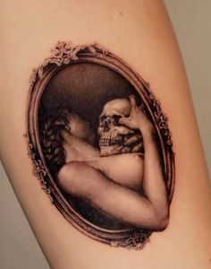 a woman's arm with a skull and frame tattoo on the back of it