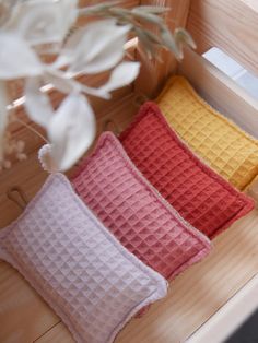 three different colored pillows sitting on top of a wooden bench next to a plant in a vase