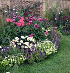 a garden filled with lots of colorful flowers next to a wooden fence in the grass