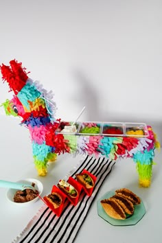 a dog made out of food on top of a white table next to plates and bowls