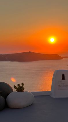 the sun is setting over an ocean with rocks in front of it and a potted plant next to it