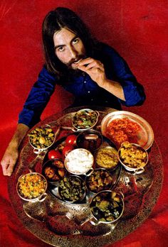 a man with long hair sitting in front of a table full of food