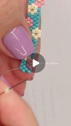 a woman with pink and blue beads on her nails holding onto a beaded bracelet