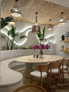 a round table surrounded by white chairs in a room with plants and potted plants