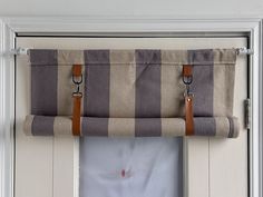 a window curtain hanging on the side of a white door with brown leather handles and straps