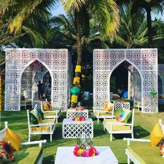 an outdoor seating area with white chairs and yellow pillows on the grass, surrounded by palm trees