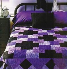 a bed with a purple and black quilt on top of it next to a night stand