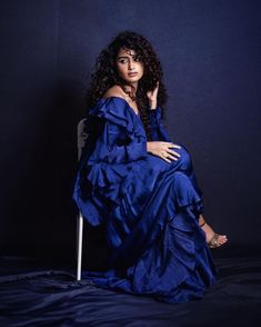 a woman in a blue dress sitting on a chair with her hand on her hip