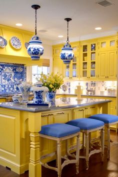 a yellow kitchen with blue and white decor on the counters, stools and cabinets