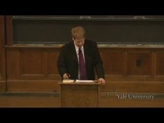 a man in a suit and tie standing at a podium with his hand on a piece of paper