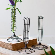 three metal vases with flowers in them sitting on a wooden table next to an open book