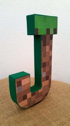 the letter j is made out of wood and has a green block on top of it