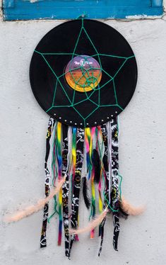 a black hat with colorful feathers hanging on the side of a white wall next to a blue window