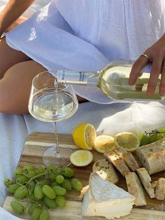 a person pouring wine into a glass next to bread and grapes