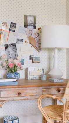 a wooden desk topped with a lamp next to a white vase filled with pink flowers