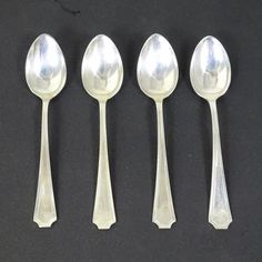 five silver spoons are lined up on a black surface