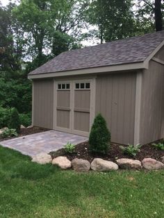 a small shed sitting in the middle of a lush green yard with rocks and trees