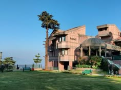 a large building sitting on the side of a lush green field next to palm trees