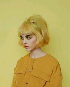 a woman with bright yellow hair and black eyeliners wearing a mustard colored shirt