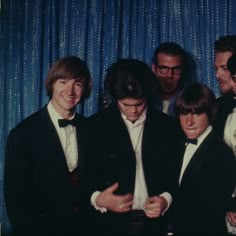 four men in tuxedos are posing for a photo with one man looking at his cell phone