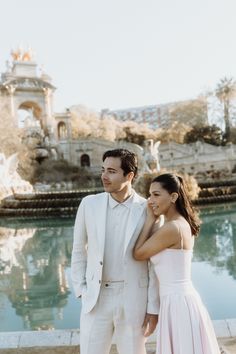 a man and woman standing next to each other in front of a fountain with water