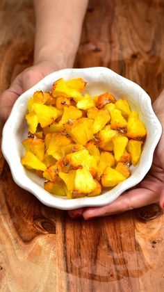 a person holding a white bowl filled with sliced pineapple on top of a wooden table