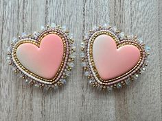 two pink heart shaped brooches are sitting on a wooden surface with beading